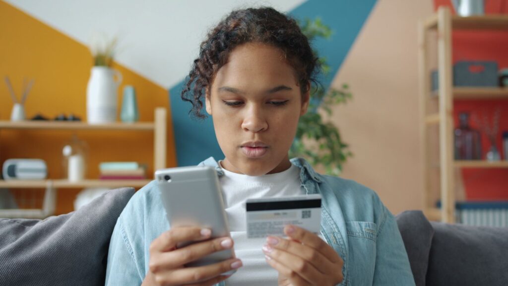 Jeune femme qui achète en ligne avec son téléphone et sa carte bancaire