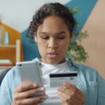 Jeune femme qui achète en ligne avec son téléphone et sa carte bancaire